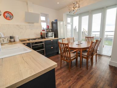 A kitchen and dining area with wooden chairs and a round table near large windows at Fairwinds in Newbiggin-By-The-Sea