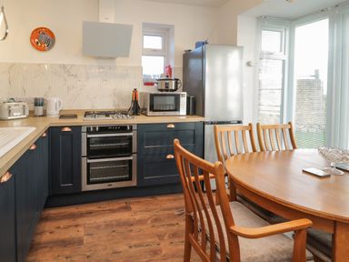 A kitchen with wooden dining table and chairs and blue lower cabinets at Fairwinds in Newbiggin-By-The-Sea