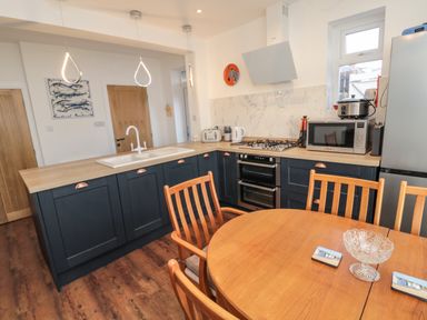 A kitchen with dark blue cabinets wooden countertops a round wooden dining table and chairs at Fairwinds in Newbiggin-By-The-Sea