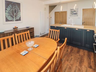 A dining area with a wooden table and chairs next to a kitchen island with a sink at Fairwinds in Newbiggin-By-The-Sea