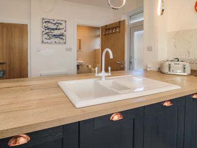 A kitchen sink with a white faucet on a wooden countertop with black cabinets and copper handles at Fairwinds in Newbiggin-By-The-Sea