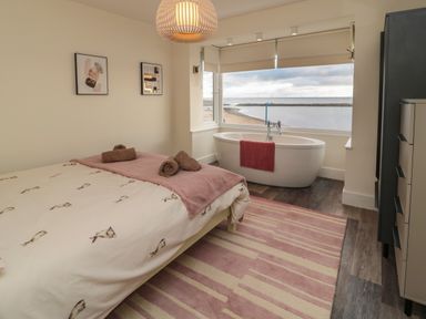 A bedroom with a bed towels and a bathtub by the window overlooking the sea at Fairwinds in Newbiggin-By-The-Sea