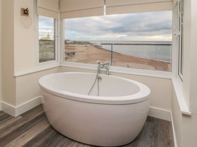 A bathroom with a freestanding bathtub and windows overlooking a beach at Fairwinds in Newbiggin-By-The-Sea