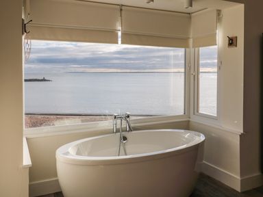A bathroom with a white bathtub under large windows overlooking the sea at Fairwinds in Newbiggin-By-The-Sea