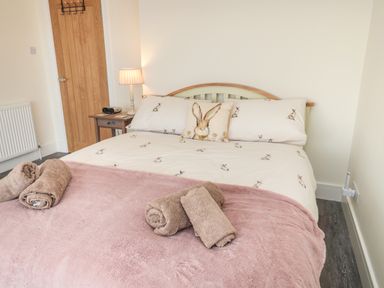 A bed with rabbit print bedding and a pink blanket with rolled towels in a bedroom at Fairwinds in Newbiggin-By-The-Sea