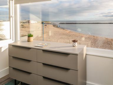 A dresser with two small plants and papers on top by a window overlooking a sandy beach and sea at Fairwinds in Newbiggin-By-The-Sea