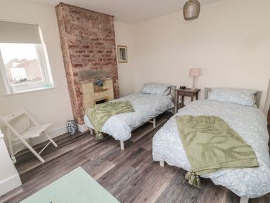 A bedroom with two single beds a small bedside table a window and an exposed brick fireplace at Fairwinds in Newbiggin-By-The-Sea