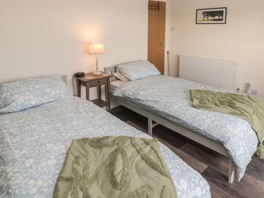 A bedroom with two single beds bedside table with lamp and clock and a framed picture on the wall at Fairwinds in Newbiggin-By-The-Sea