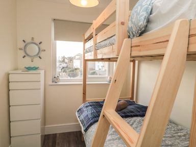 A bedroom with a wooden bunk bed a white chest of drawers a window with a blind and a decorative mirror at Fairwinds in Newbiggin-By-The-Sea