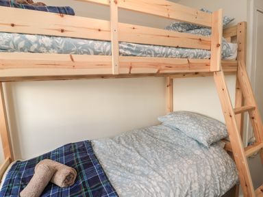 A bunk bed with light wooden frame bedding with floral patterns and a plaid blanket with rolled towels at Fairwinds in Newbiggin-By-The-Sea