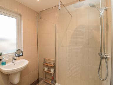 A bathroom with a wall-mounted sink soap dispenser small mirror and a shower with glass partition at Fairwinds in Newbiggin-By-The-Sea