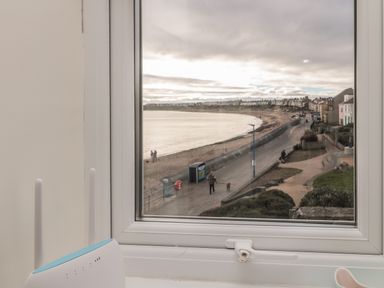 A window with a view of a beach promenade with people walking and houses along the street at Fairwinds in Newbiggin-By-The-Sea