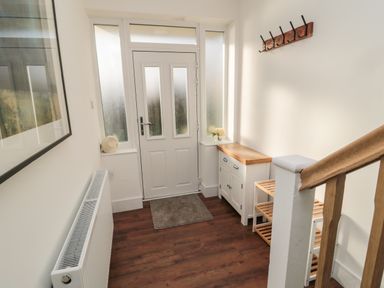 A hallway with a white door, a wooden shoe rack, a small cabinet, a coat rack on the wall, and a radiator at Fairwinds in Newbiggin-By-The-Sea