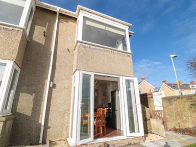 The exterior of a two-story house with open glass doors revealing a kitchen and dining area at Fairwinds in Newbiggin-By-The-Sea