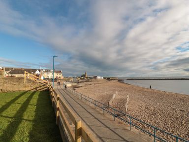 A sandy beach with a paved walkway and buildings in the background at Fairwinds in Newbiggin-By-The-Sea