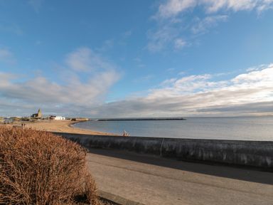 A beach with a stone seawall and a view of the ocean at Fairwinds in Newbiggin-By-The-Sea