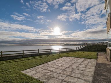 A garden with a paved patio a wooden fence and a view of the sea at Fairwinds in Newbiggin-By-The-Sea