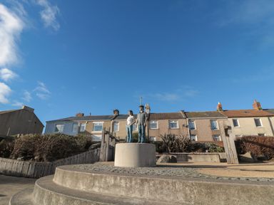 A sculpture of a man and woman on a circular concrete pedestal in a residential area at Fairwinds in Newbiggin-By-The-Sea