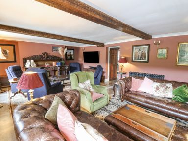A living room with leather sofas green armchair blue chairs wooden beams and framed pictures on walls at Ty Sinsir in Tretower