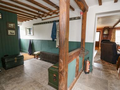 An entrance hallway with wooden beams a green wooden chest a radiator coats hanging on the wall and a fire extinguisher at Ty Sinsir in Tretower