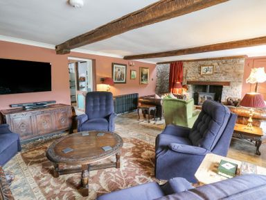 A living room with wooden beams on the ceiling blue armchairs wooden coffee table and stone fireplace at Ty Sinsir in Tretower