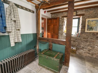 A hall with a green wooden chest coats hanging on hooks a radiator and a stone wall with a small window at Ty Sinsir in Tretower