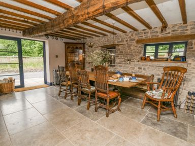 A dining room with wooden table and chairs exposed beam ceiling stone walls and large window at Ty Sinsir in Tretower