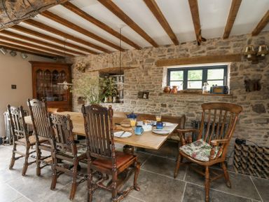A dining room with a wooden table set for breakfast and wooden chairs at Ty Sinsir in Tretower