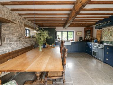A kitchen with a wooden dining table and chairs stone walls and blue cabinets at Ty Sinsir in Tretower