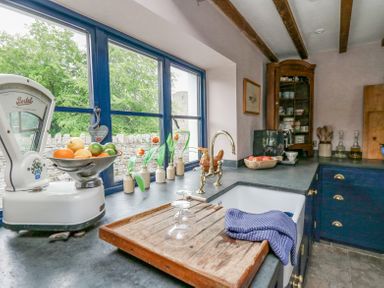 A kitchen countertop with a vintage scale holding fruit a sink with a drying rack and glasses flowers in small vases and cabinets in a kitchen at Ty Sinsir in Tretower