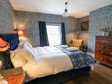 A bedroom with a large bed a wooden chest of drawers an upholstered chair and floral wallpaper at Ty Sinsir in Tretower