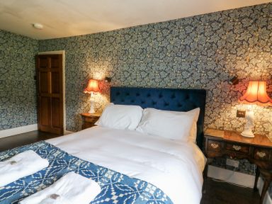 A bedroom with a bed white linens blue patterned blanket two bedside tables with lamps and floral wallpaper at Ty Sinsir in Tretower