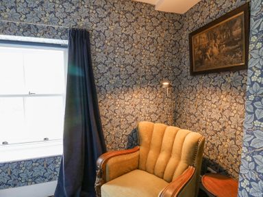 A corner with a beige armchair a side table floor lamp and floral wallpaper at Ty Sinsir in Tretower