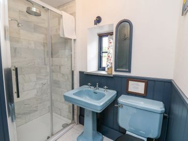 A bathroom with a blue sink and toilet a glass shower enclosure and a small window at Ty Sinsir in Tretower