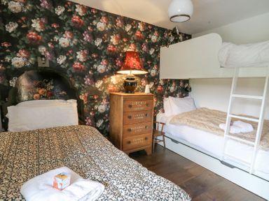 A bedroom with a single bed a bunk bed a wooden chest of drawers with a lamp and floral wallpaper at Ty Sinsir in Tretower