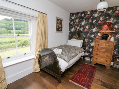 A bedroom with a single bed floral wallpaper wooden chest of drawers and window with yellow curtains at Ty Sinsir in Tretower