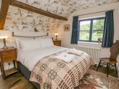 A bedroom with a double bed two bedside tables with lamps a window with blue curtains and a wooden chair at Ty Sinsir in Tretower