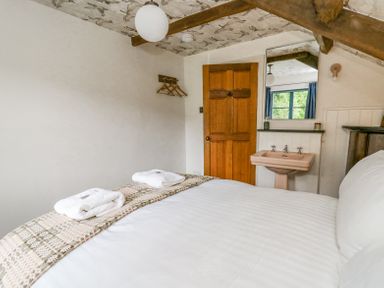 A bedroom with a bed, folded towels, a wooden door, a pink sink, a wall mirror, and a ceiling with patterned wallpaper at Ty Sinsir in Tretower