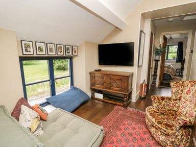 A small living room with a wooden cabinet and wall mounted TV a green sofa and a patterned armchair with a red rug at Ty Sinsir in Tretower