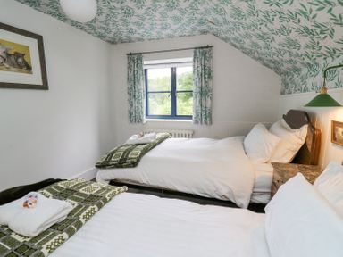 A bedroom with two beds green patterned blankets window with green patterned curtains and wall art at Ty Sinsir in Tretower