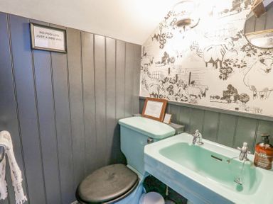 A bathroom with a turquoise toilet and sink dark grey panel walls and sheep wallpaper at Ty Sinsir in Tretower