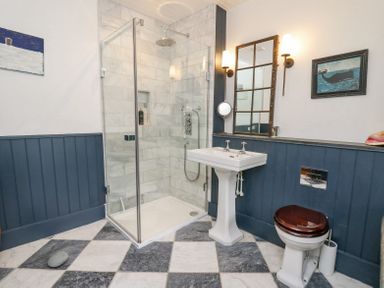 A bathroom with a glass shower enclosure a pedestal sink and a toilet with a wooden seat at Ty Sinsir in Tretower