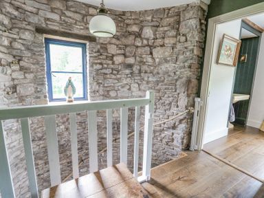 A stone wall stairwell with a white wooden railing and a statue by the window at Ty Sinsir in Tretower