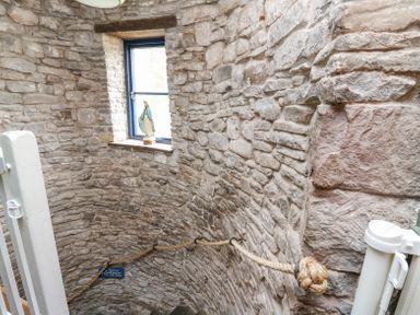 A stone staircase with a rope handrail and a statue on a window sill at Ty Sinsir in Tretower
