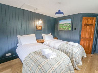 A bedroom with two single beds with checkered blankets and white towels on top at Ty Sinsir in Tretower