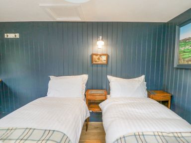 A bedroom with two single beds white bedding wooden bedside tables and blue paneled walls at Ty Sinsir in Tretower