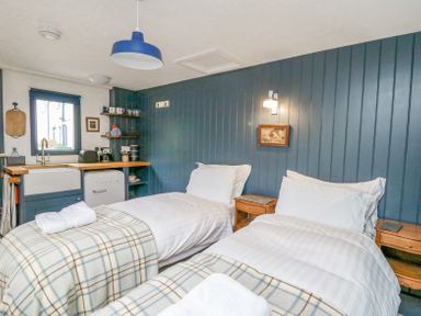 A bedroom with two single beds a wooden nightstand a small kitchenette and a window at Ty Sinsir in Tretower
