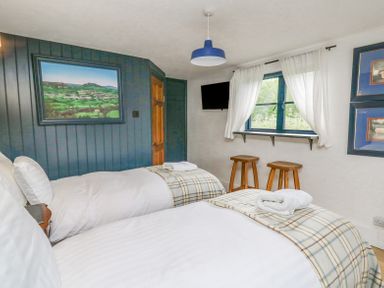 A bedroom with two single beds blue paneled wall painting two wooden stools under a window with white curtains at Ty Sinsir in Tretower