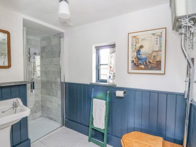 A bathroom with a glass shower enclosure a white sink a small window a towel on a green ladder and a wooden toilet seat at Ty Sinsir in Tretower