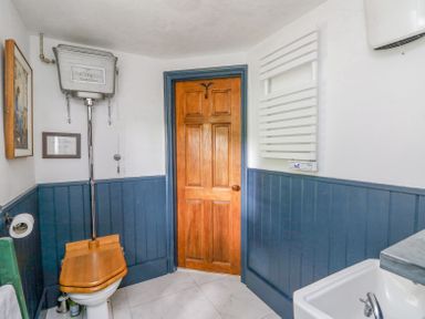 A bathroom with a wooden toilet seat a high level cistern wooden door and a white sink with blue paneling on walls at Ty Sinsir in Tretower